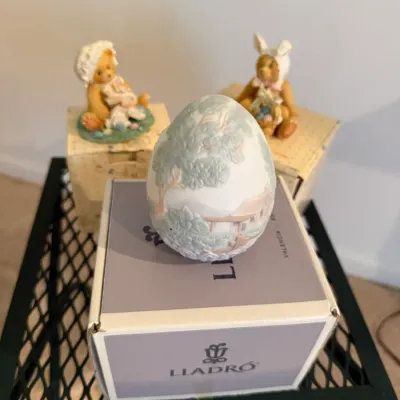 Sale Photo Thumbnail #22: Lladro porcelain Easter egg figurine displayed on its original box alongside two small teddy bear figurines.