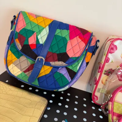 Sale Photo Thumbnail #54: Quilted colorful geometric crossbody bag with blue trim and buckle detail, sitting alongside other accessories including a gold metallic clutch.