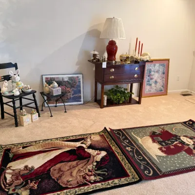 Sale Photo Thumbnail #61: Collection of home decor items including seasonal holiday area rugs, framed artwork, a dark wood drop-leaf side table topped with a red lamp, and a black ladder-back chair.
