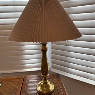 Sale Photo Thumbnail #9: Polished brass table lamp featuring a contoured baluster body and a pleated fabric lampshade, sitting on a wooden tabletop.