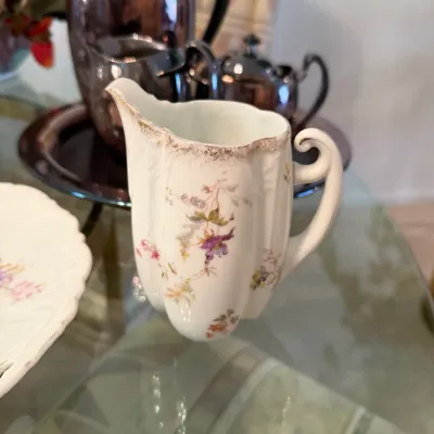 Sale Photo Thumbnail #46: Antique porcelain creamer with delicate floral transfers and gold trim accents, sitting on a glass tabletop.
