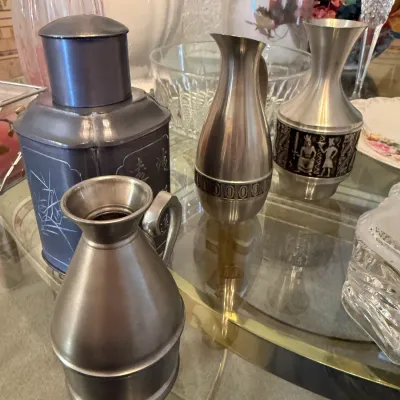 Sale Photo Thumbnail #42: Collection of pewter tableware items, including small pitchers with etched decorative bands and a canister with Asian-inspired etched motifs.