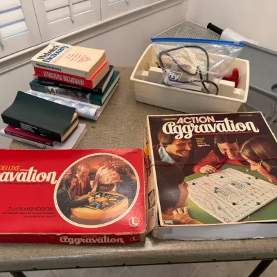 Sale Photo Thumbnail #71: Vintage board games including Deluxe Aggravation and Lakeside's Action Aggravation, along with a stack of books and a plastic storage bin.