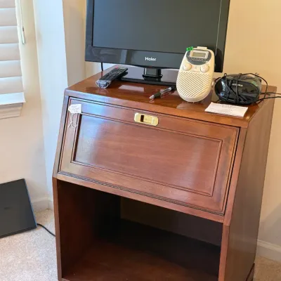 Sale Photo Thumbnail #56: Solid wood slant-front secretary desk topped with electronics, including a Haier LCD television, remote control, and portable radios.