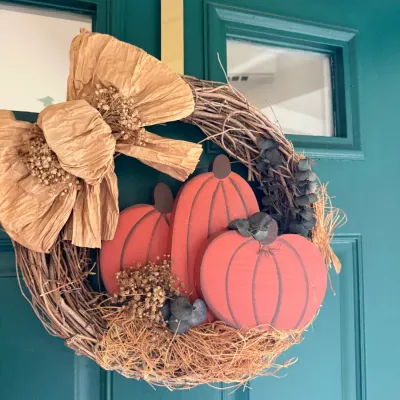 Sale Photo Thumbnail #20: Autumn grapevine door wreath featuring three painted wooden pumpkins, a large paper bow, and dried floral accents.