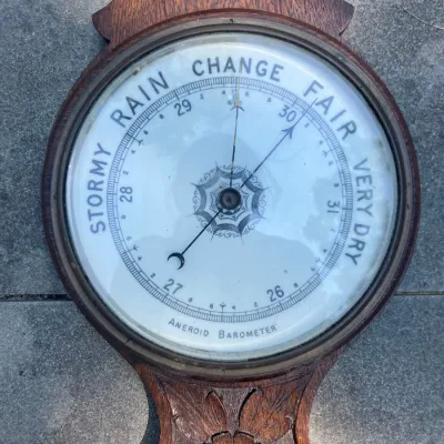 Vintage carved wooden aneroid barometer with a detailed white dial and brass bezel.