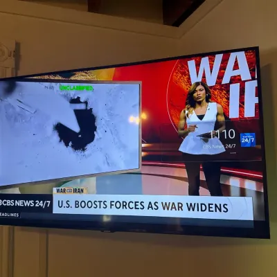 Wall-mounted modern flat screen television displaying a news broadcast.