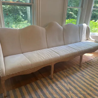French Provincial style long banquette sofa with light beige linen upholstery, camelback silhouette, and light oak cabriole legs.