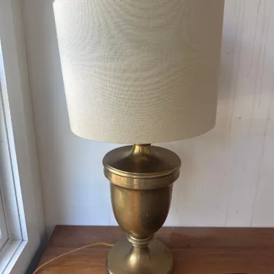 Mid-century brass urn-form table lamp topped with a beige drum lampshade.