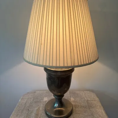 Traditional urn-style metal table lamp with a dark, tarnished patina and a cream pleated fabric lampshade.