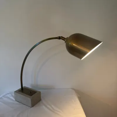 Mid-century modern brass desk lamp featuring a curved neck, a bullet-style cone shade, and a heavy rectangular concrete base.