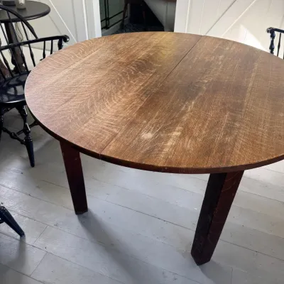 Round quarter-sawn oak dining table featuring a split top for leaves and straight legs, showing light surface wear.