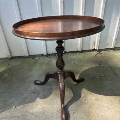 Vintage mahogany oval tilt-top tea table with raised gallery edge, carved pedestal stem, and tripod cabriole legs ending in pad feet.