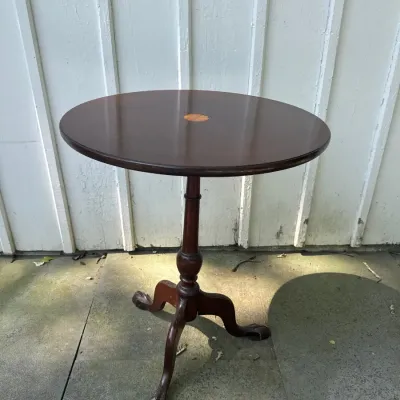 Traditional dark mahogany tilt-top or accent table featuring a round top with a central starburst inlay and a turned pedestal base with...