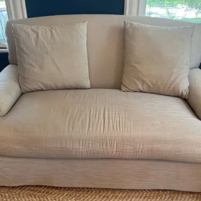 Contemporary beige upholstered chair-and-a-half with matching throw pillows and a skirted base.