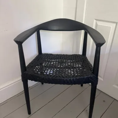 Black wooden armchair in Hans Wegner style featuring a curved backrest and woven cord seat.