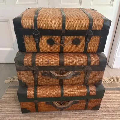 Stack of three vintage woven rattan or wicker trunks with metal hardware and leather accents.
