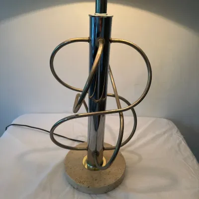 Mid-century modern table lamp featuring a chrome central column surrounded by looped metal tubing, resting on a round travertine base.