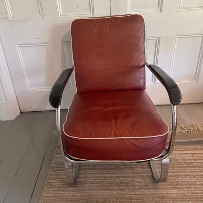 Vintage Art Deco style chrome cantilever armchair featuring reddish-brown vinyl cushions with white piping and dark armrests.