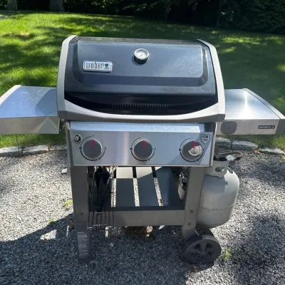 Weber Spirit II three-burner liquid propane gas grill with fold-down side tables and attached propane tank.