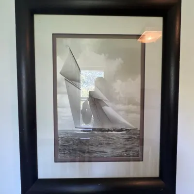 Framed black and white nautical photograph of a sailboat under way, double matted and set in a thick dark wood frame.