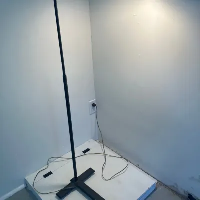 Modernist black metal adjustable floor lamp with a T-shaped base and rectangular hood shade, shown plugged in and illuminated.