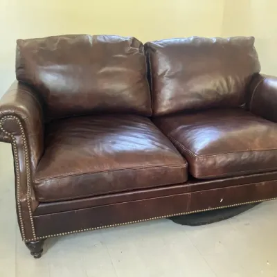 Dark brown leather loveseat featuring rolled arms, brass nailhead trim along the base and arms, and turned wooden feet.
