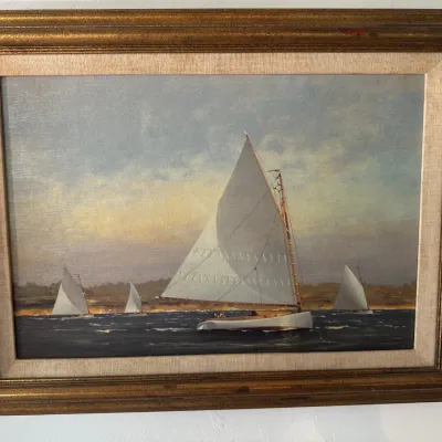 Framed nautical oil painting depicting sailboats on open water, set within a gilt wood frame with a linen liner.