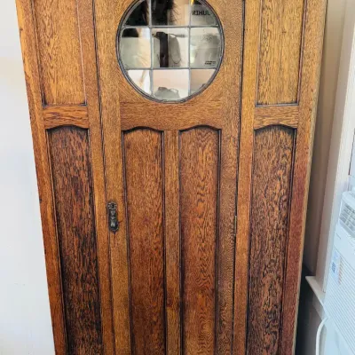 Antique Arts and Crafts style oak armoire featuring a central circular leaded glass window, paneled wood construction, and dark hardware.