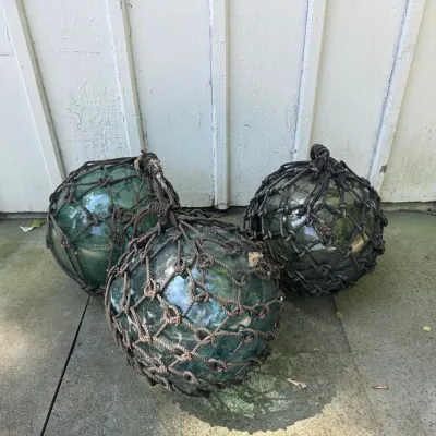 Trio of vintage Japanese green glass fishing floats enclosed in weathered rope netting.
