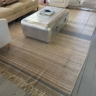 Restoration Hardware style aviator aluminum trunk coffee table, paired with a large neutral woven area rug featuring fringed edges.