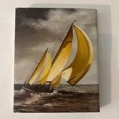Framed oil painting depicting a sailboat with vibrant yellow sails navigating choppy waters, signed Elliot in the lower right corner.