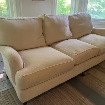 Traditional cream-colored upholstered three-cushion sofa with rolled arms and caster feet.
