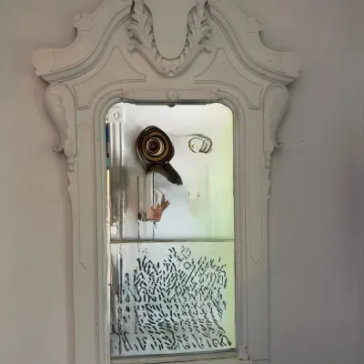 Vintage white-painted wooden wall mirror with ornate carved pediment top and distressed mirror glass.