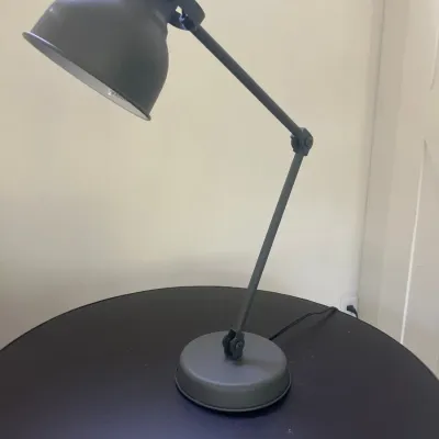 Modern dark grey metal adjustable desk lamp on a matching round table.