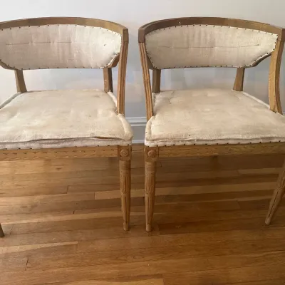Pair of Neoclassical style barrel-back accent chairs featuring fluted legs, carved wood frames, and off-white muslin upholstery.