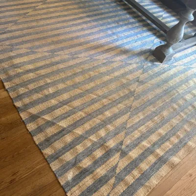 Large contemporary flat-weave area rug featuring a geometric striped pattern in blue and natural jute tones.