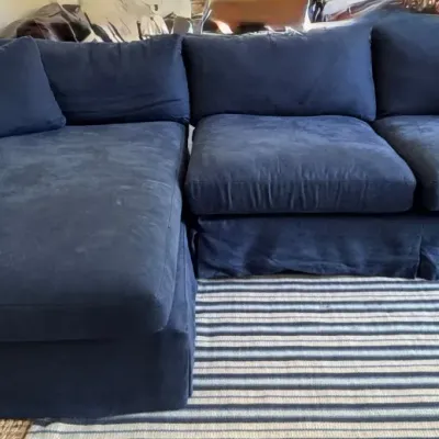 Contemporary navy blue sectional sofa with a left-facing chaise and matching throw pillows, featuring slipcover-style fabric skirts.