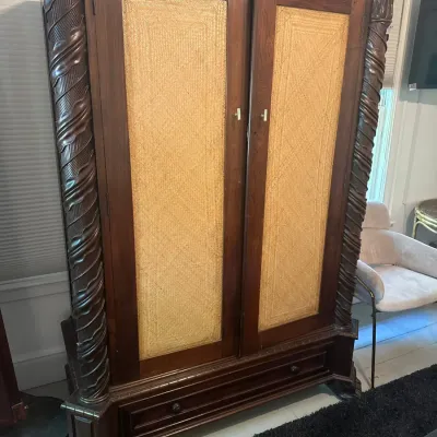 Large tropical plantation-style armoire featuring woven grass cloth door panels, carved rope-twist corner columns, and a lower drawer.