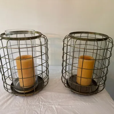 Pair of modern industrial brass wire cage hurricane candle holders, featuring glass inserts with yellow pillar candles.