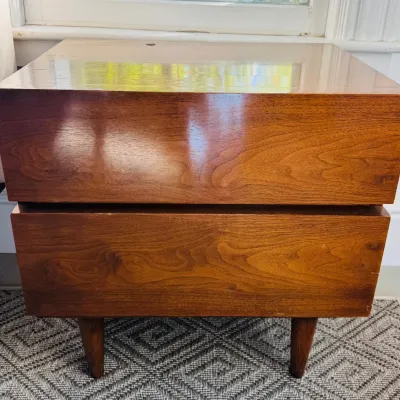 Mid-century modern two-drawer wooden nightstand with tapered legs and integrated recessed drawer pulls.