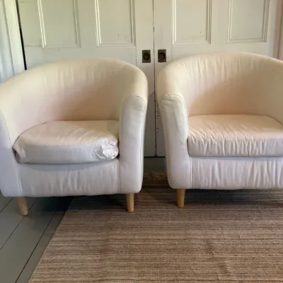 Pair of contemporary modern barrel tub armchairs upholstered in off-white fabric with light wood tapered legs.