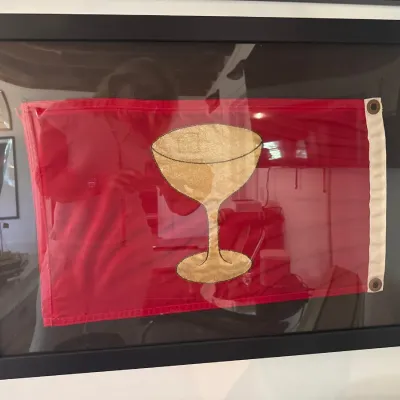 Framed red nautical cocktail flag featuring a gold coupe glass graphic, mounted in a black wooden frame.