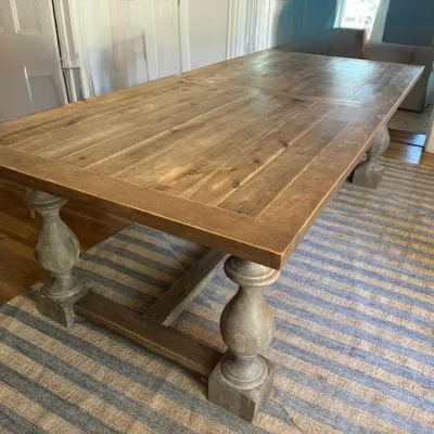 Rustic farmhouse-style wooden dining table featuring a plank-style top and carved baluster trestle legs.