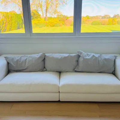 Sale Photo Thumbnail #5: Contemporary off-white modern sofa featuring wide track arms and light gray accent back pillows, set against a bay window view.