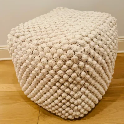 Sale Photo Thumbnail #27: Cream-colored bohemian chunky knit cube pouf Ottoman resting on light wood flooring.
