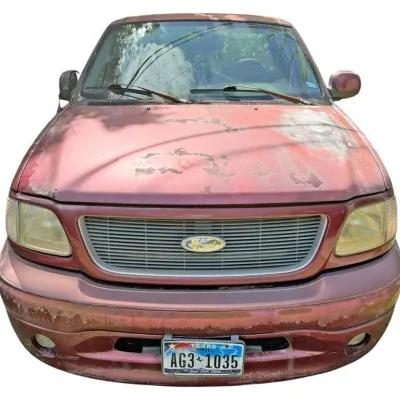Front view of a late 1990s to early 2000s maroon Ford truck displaying heavy clear coat peeling, sun damage on the hood, and faded...