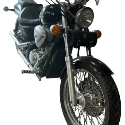 Black Honda Shadow cruiser motorcycle featuring a front windshield, handlebars with attached pouch, and wire-spoke front wheel.