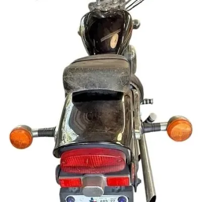 Rear view of a black cruiser motorcycle featuring dual side mirrors, a tall windshield, amber turn signals, and a Texas license plate.