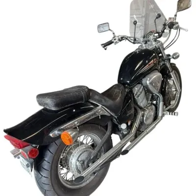 Black Honda Shadow cruiser motorcycle featuring chrome dual exhaust pipes, spoked wheels, dual side mirrors, and a clear windshield.